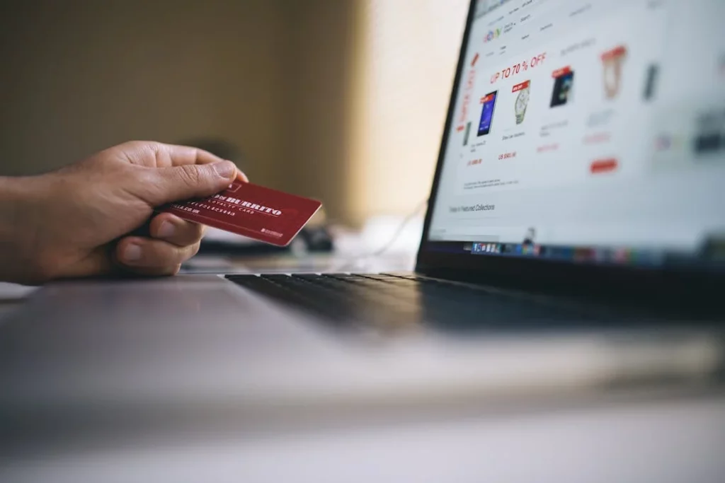 A person on a laptop, holding a credit card while browsing products. This image represents AI ecommerce integration, depicting how artificial intelligence analyzes user behavior and preferences to personalize product recommendations and streamline the online shopping experience.