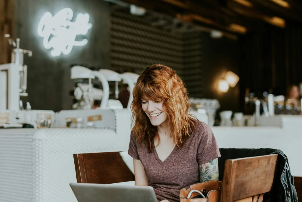 A woman smiling while using her laptop, immersed in online shopping or browsing eCommerce platforms. This image illustrates the significance of TikTok eCommerce marketing and highlights the role of AI in enhancing consumer engagement and creating a more personalized shopping experience.