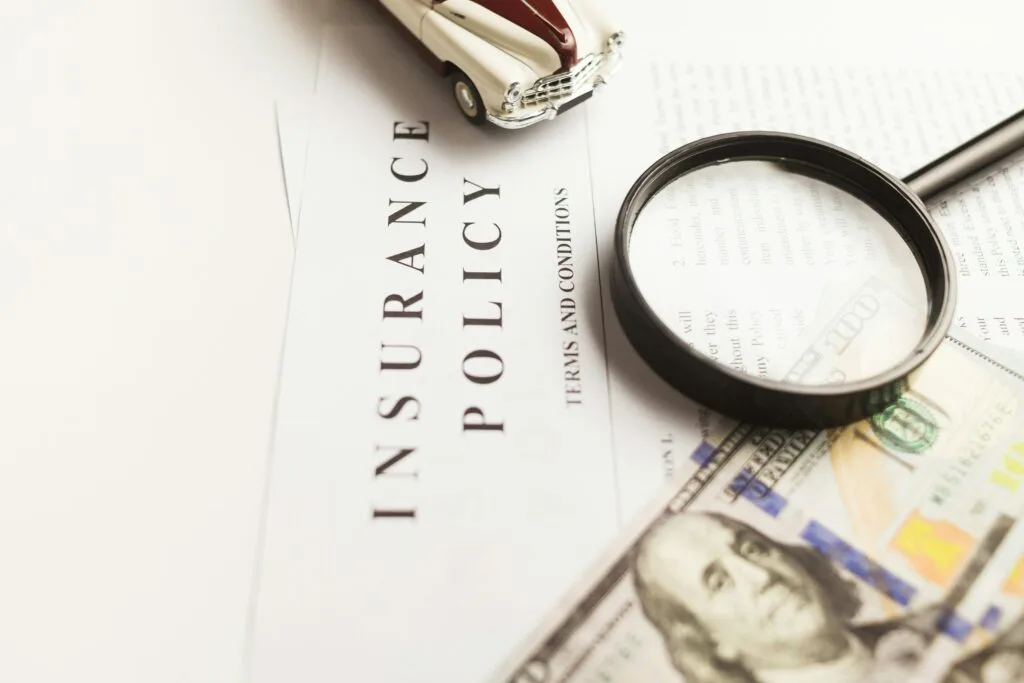 Insurance policy document with magnifying glass, dollar bills, and a car model, representing financial planning and protection for small businesses.