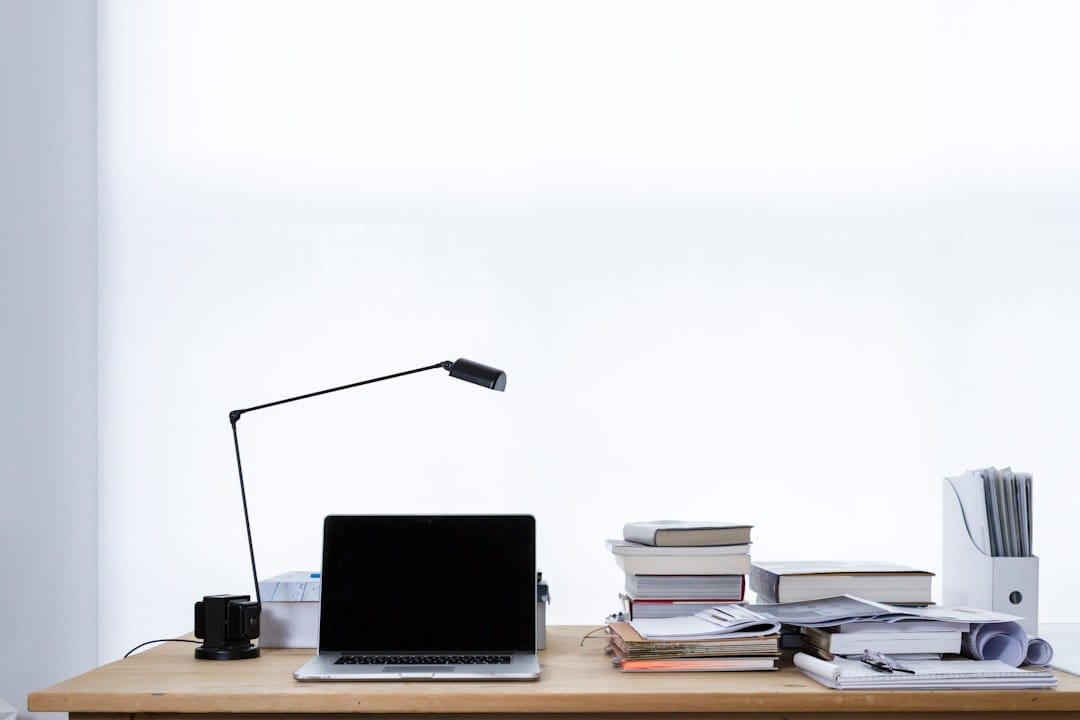 Minimalist office desk with a laptop, stack of books, and a modern lamp, emphasizing effective workspace for strategizing confirmation email templates.