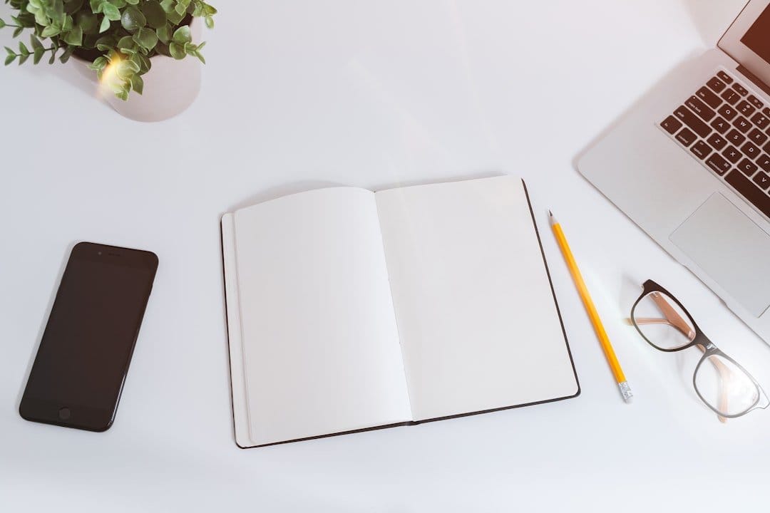 Alt text: Workspace setup with an open notebook, phone, laptop, pencil, and glasses, symbolizing UX design strategy planning.