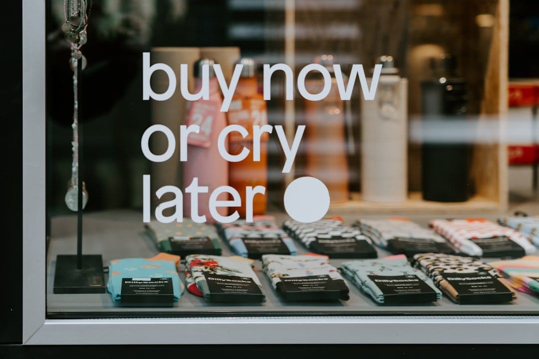 Retail store window displaying eCommerce news with buy now or cry later sign and product merchandise