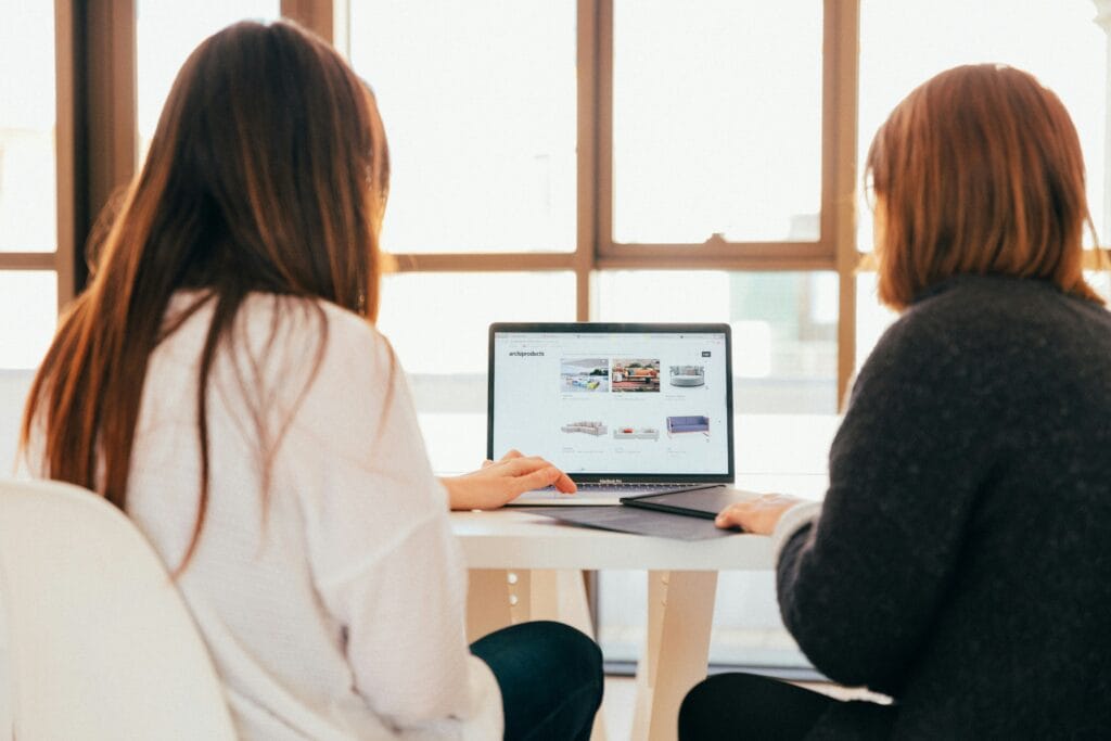 Two women surfing the web for couches after reading about sales in eCommerce news.