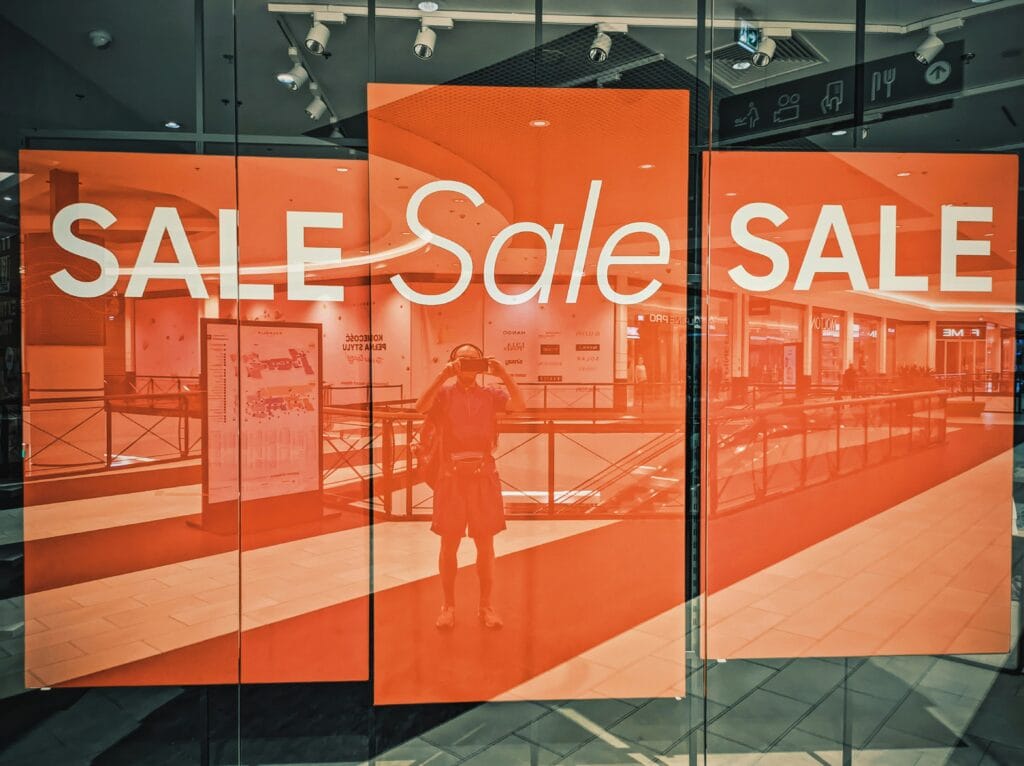 Retail store window displays sale signs with 70% and 30% discounts on shoes amid eCommerce news about tariff disruptions